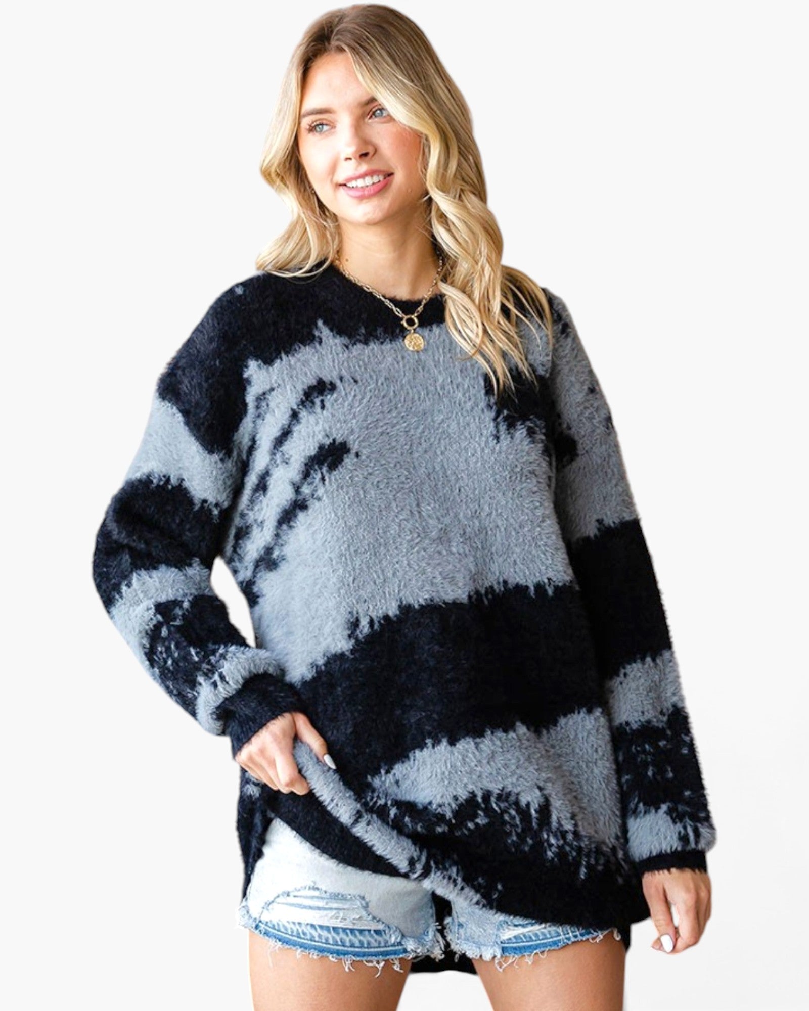 A woman wearing a fuzzy long-sleeve sweater with a black and gray tie-dye pattern, paired with light-wash denim shorts, against a plain white background.