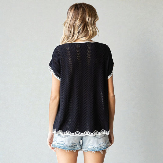 Woman wearing a black and white patterned top with denim shorts on a plain background