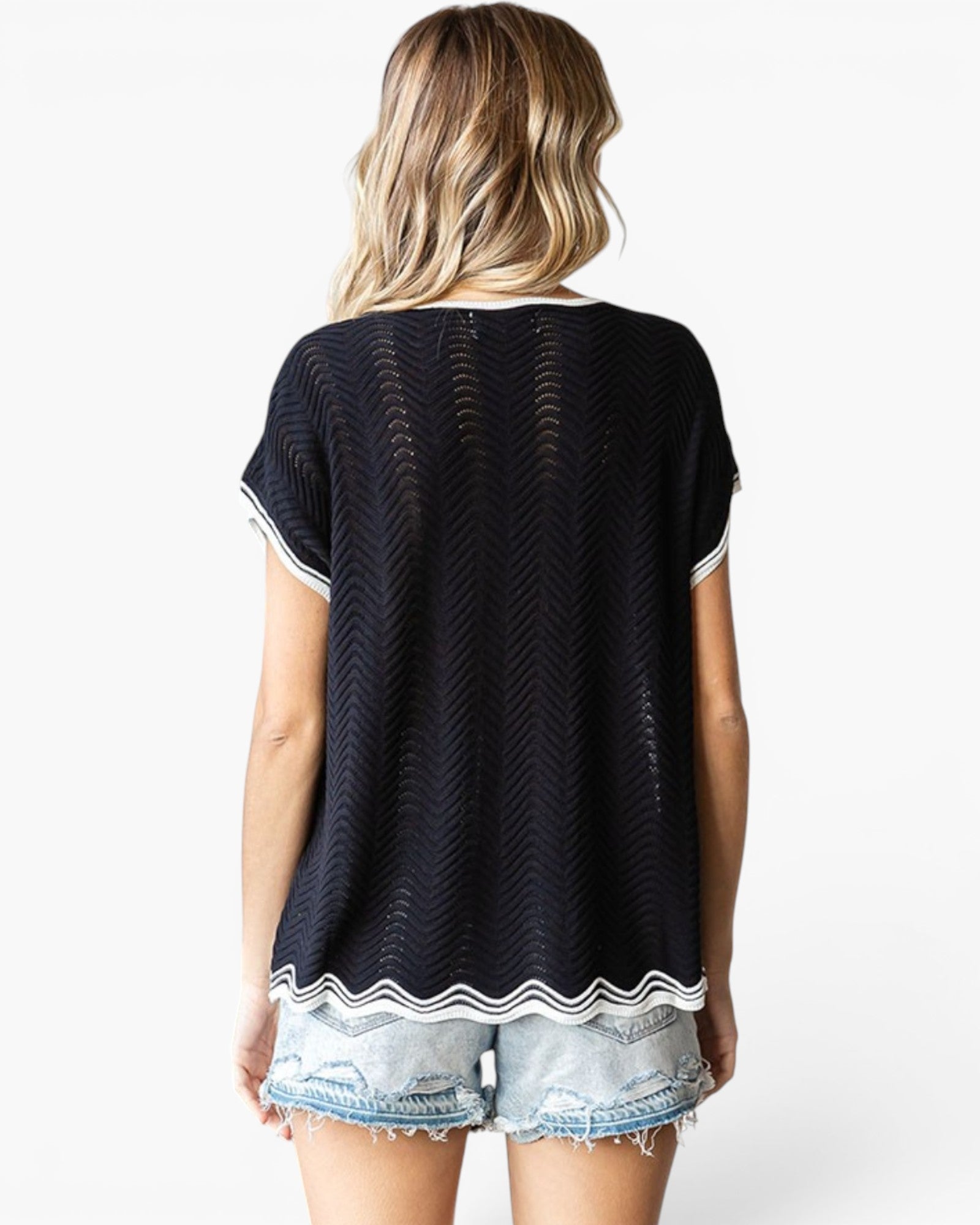A woman shown from the back wearing a black short-sleeve knit top with white contrast trim and light-wash denim shorts against a plain white studio background.