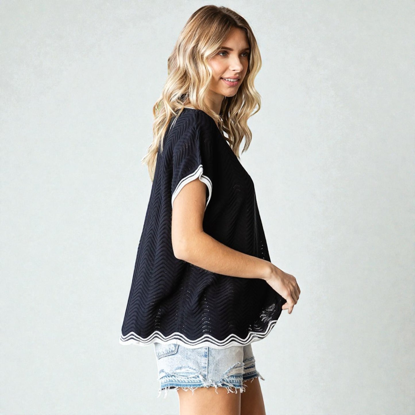 Woman wearing a black sleeveless top with white trim on a plain background