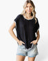 A woman modeling a black short-sleeve top with a subtle chevron knit pattern and white contrast trim, paired with light-wash denim shorts, against a plain white studio background.