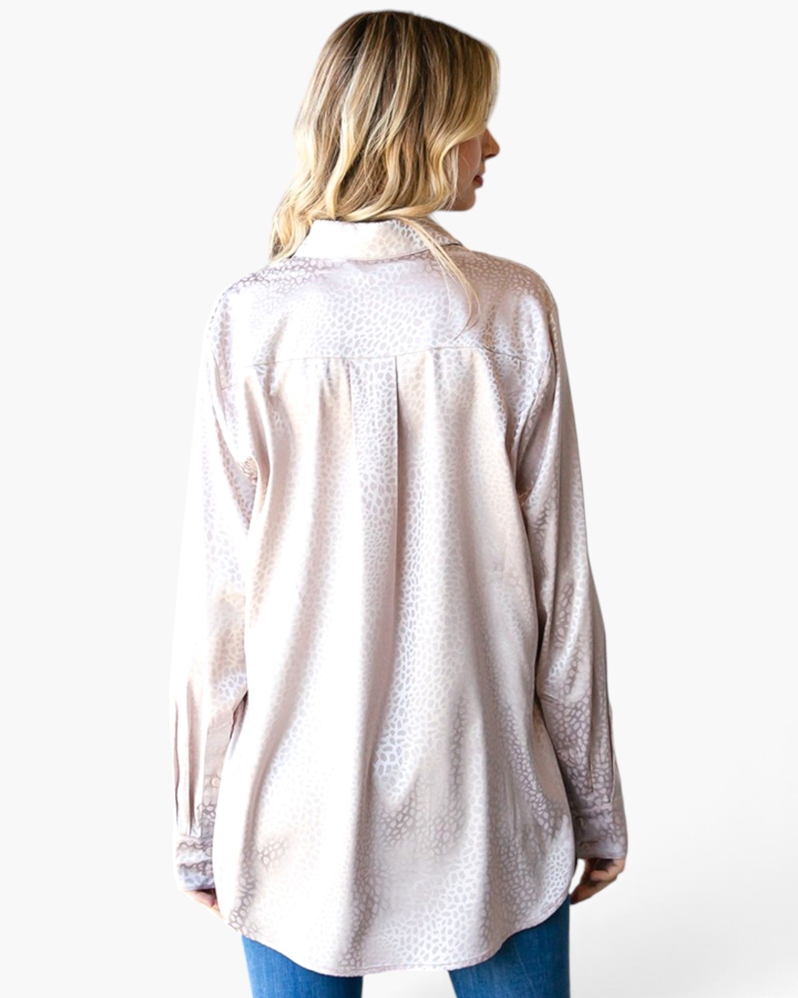 A woman shown from the back wearing a light pink long-sleeve button-up shirt with a subtle textured pattern, paired with blue jeans, against a plain white background.