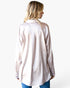 A woman shown from the back wearing a light pink long-sleeve button-up shirt with a subtle textured pattern, paired with blue jeans, against a plain white background.