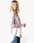 A woman wearing a light beige long-sleeve button-up shirt with a subtle dotted pattern and sheer lace cuffs, paired with blue jeans, photographed against a solid white background.
