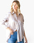 A woman modeling a loose, light pink satin button-up shirt with a subtle white pattern, tucked into blue jeans against a plain white background.