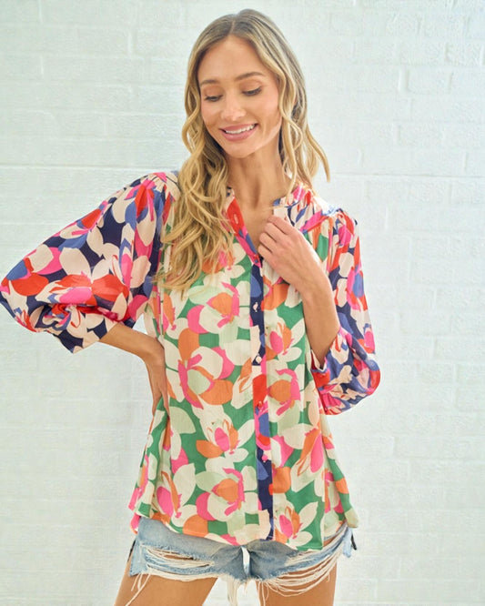 Woman wearing a colorful floral blouse against a white brick wall.