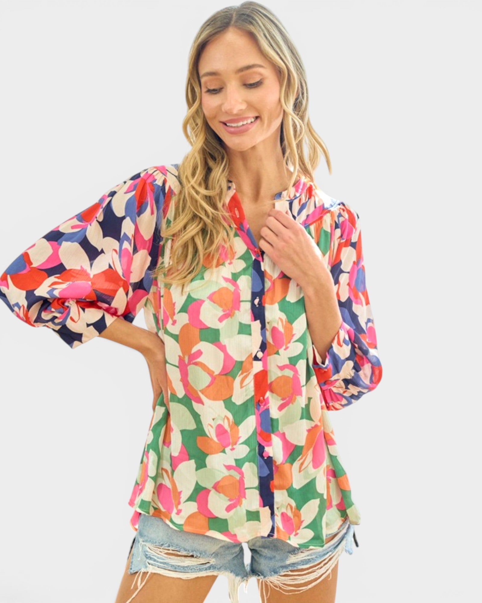 A woman wearing a colorful floral long-sleeve blouse with puff sleeves and denim shorts, posing against a light gray background.