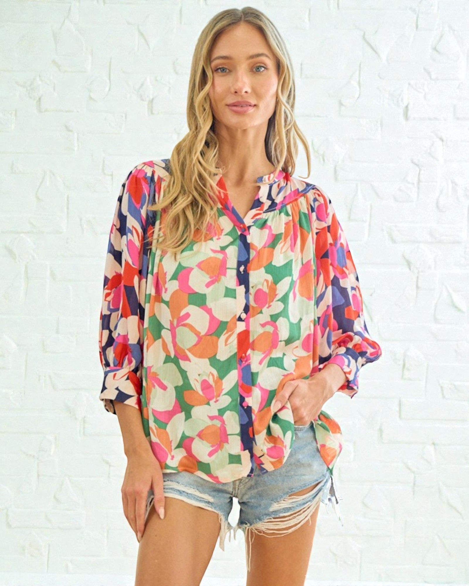 Woman wearing a colorful floral blouse against a white textured wall