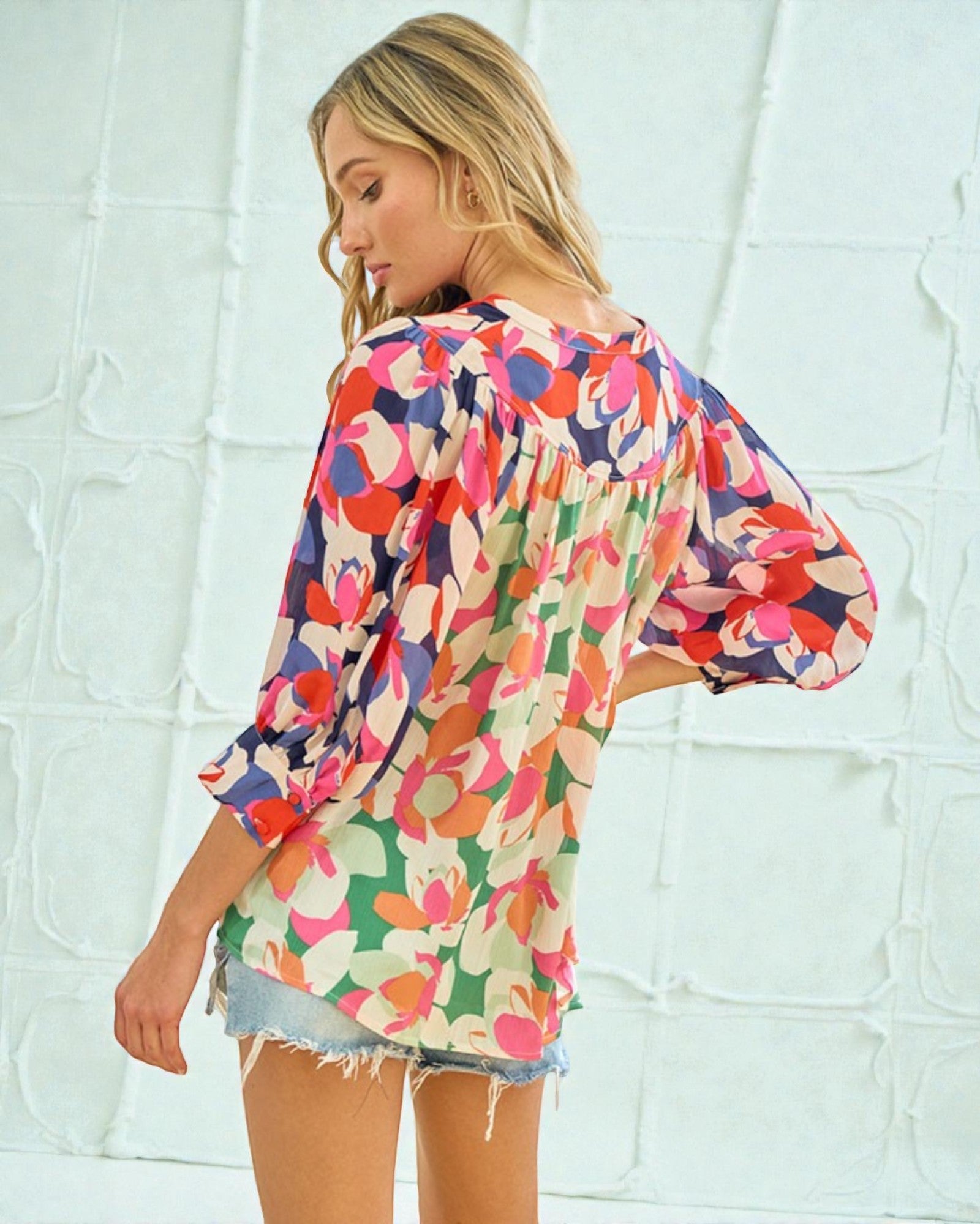 Woman wearing a colorful floral kimono against a light textured wall.