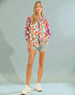 Woman wearing a colorful floral shirt and denim shorts on a plain background