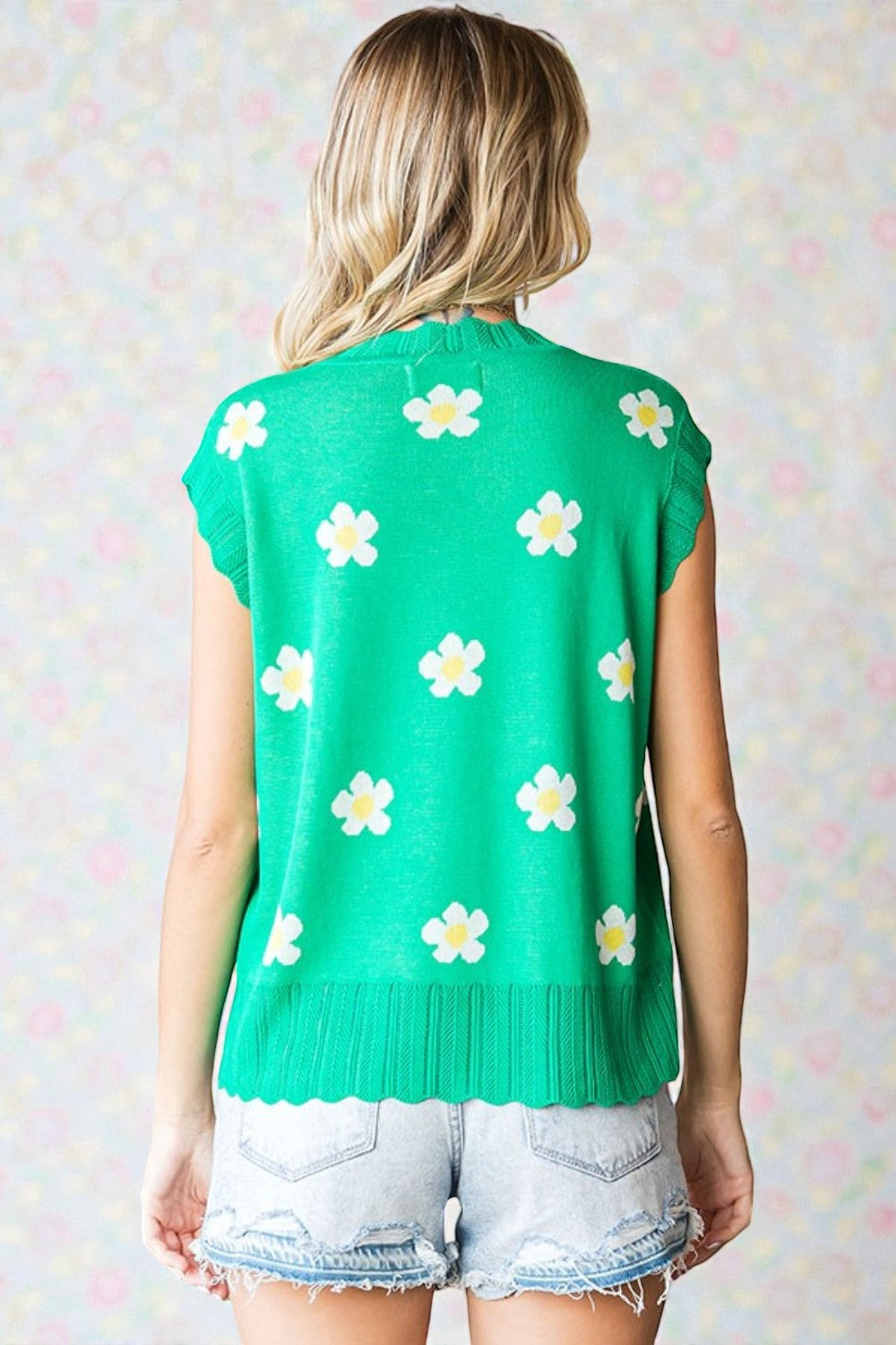 Green sleeveless sweater with white floral patterns worn by a person against a light background