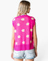 A woman shown from the back wearing a bright pink sleeveless knit top with a scalloped hem and an allover white daisy pattern, paired with light-wash denim shorts against a plain white background.