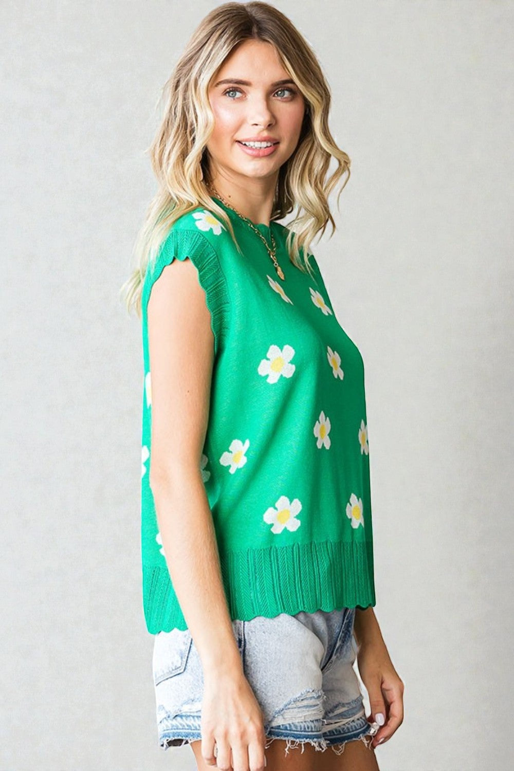Woman wearing a green sleeveless sweater with floral patterns against a plain background