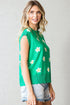 Woman wearing a green sleeveless sweater with floral patterns against a plain background