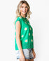 A woman wearing a bright green sleeveless knit top with a white and yellow daisy pattern, paired with denim shorts, against a plain white background.