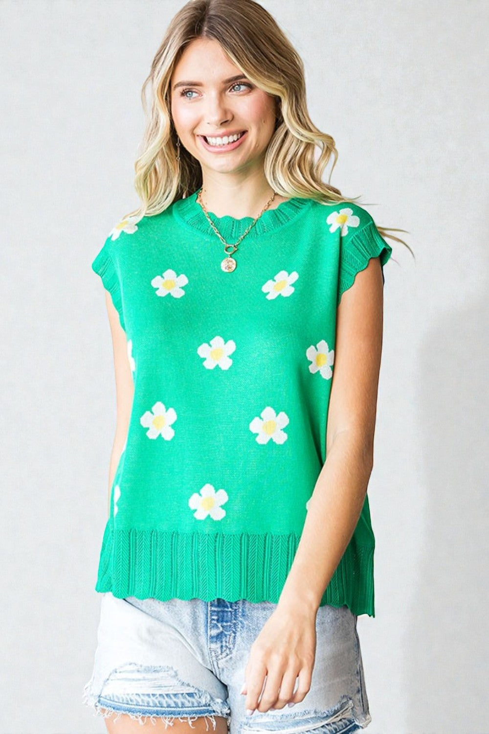 Woman wearing a green sleeveless top with white floral patterns against a plain background