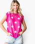 A woman wearing a bright pink sleeveless knit top with a white and yellow daisy pattern, paired with light-wash denim shorts, against a plain white background.
