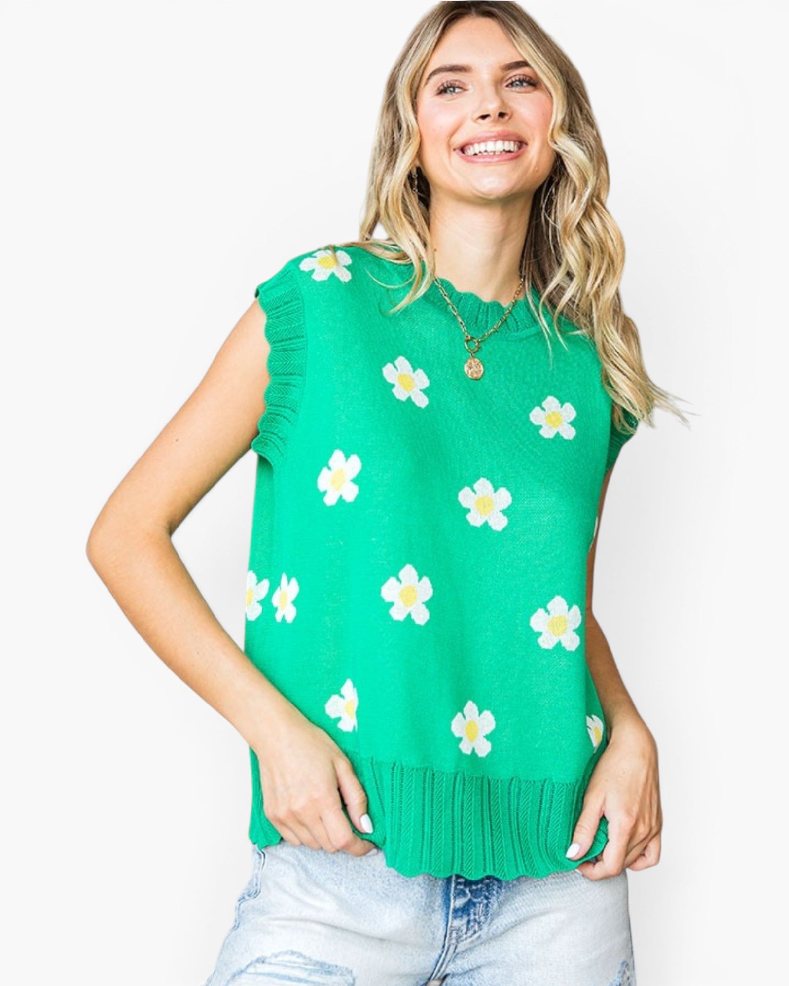 A woman wearing a bright green sleeveless knit top with a white and yellow flower pattern, paired with light-wash jeans, against a plain white background.