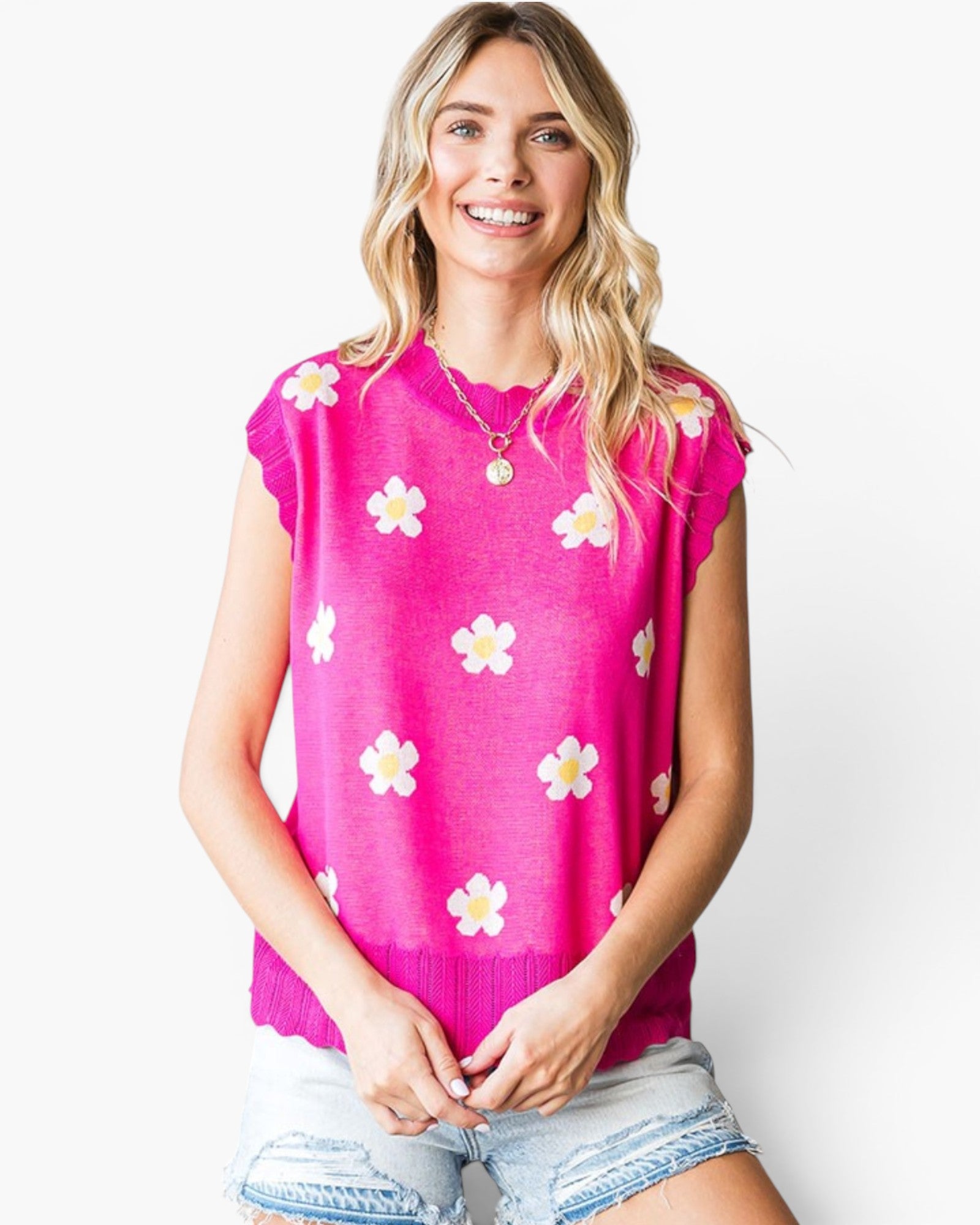 A woman wearing a bright pink knit top with a white daisy pattern, paired with light-wash denim shorts, against a plain white background.