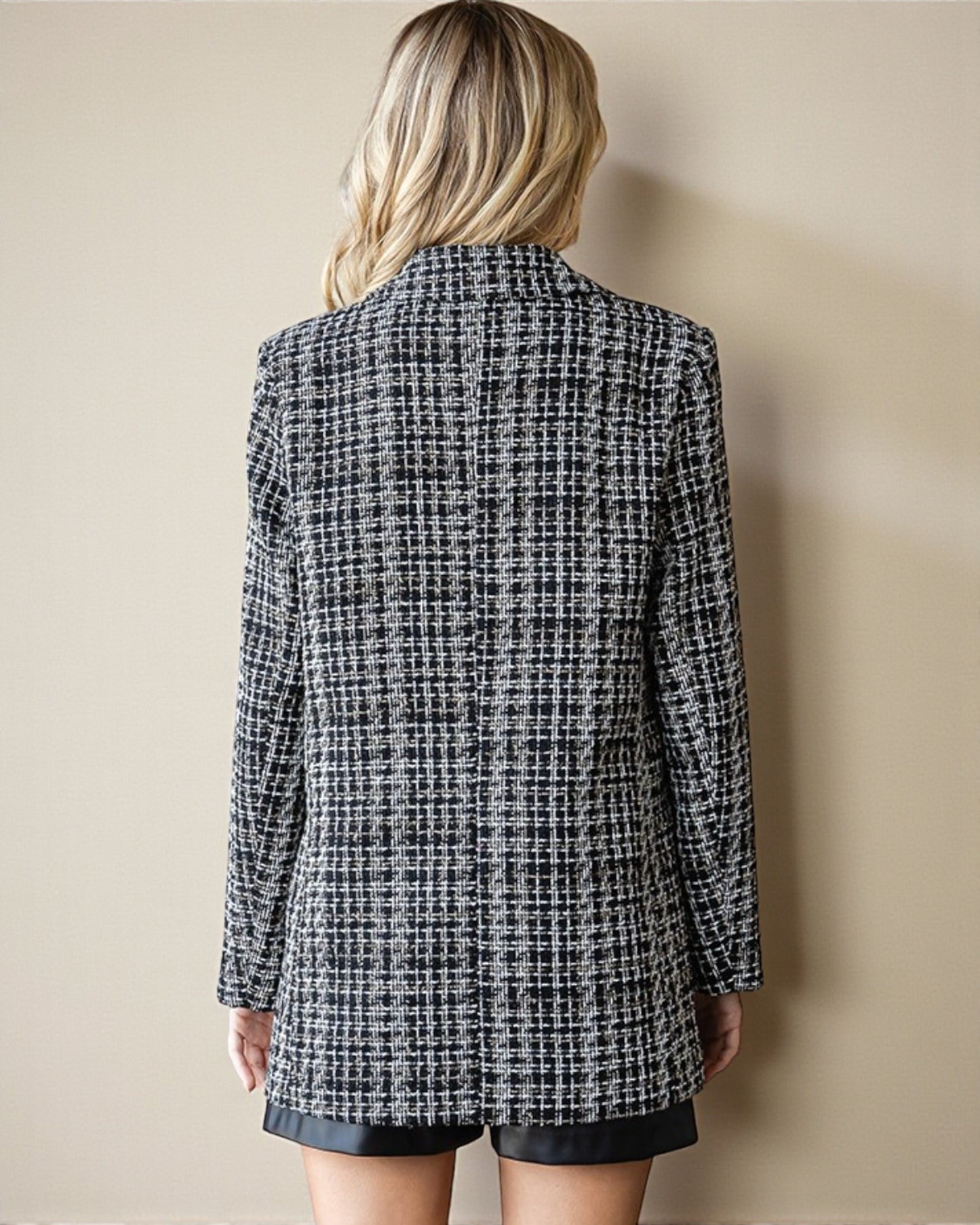 Person wearing a black and white checkered blazer against a beige wall