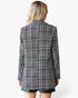 A woman shown from the back wearing a black and white tweed blazer with black leather shorts against a plain white background.
