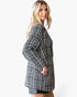 A woman wearing a black and white houndstooth tweed long-sleeve tunic dress, shown from a side-back angle against a plain white studio background.