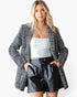 A woman modeling a black and white houndstooth blazer over a white tube top and black faux leather shorts, set against a plain white studio background.