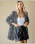 Woman wearing a checkered blazer over a white top and black leather shorts on a beige background