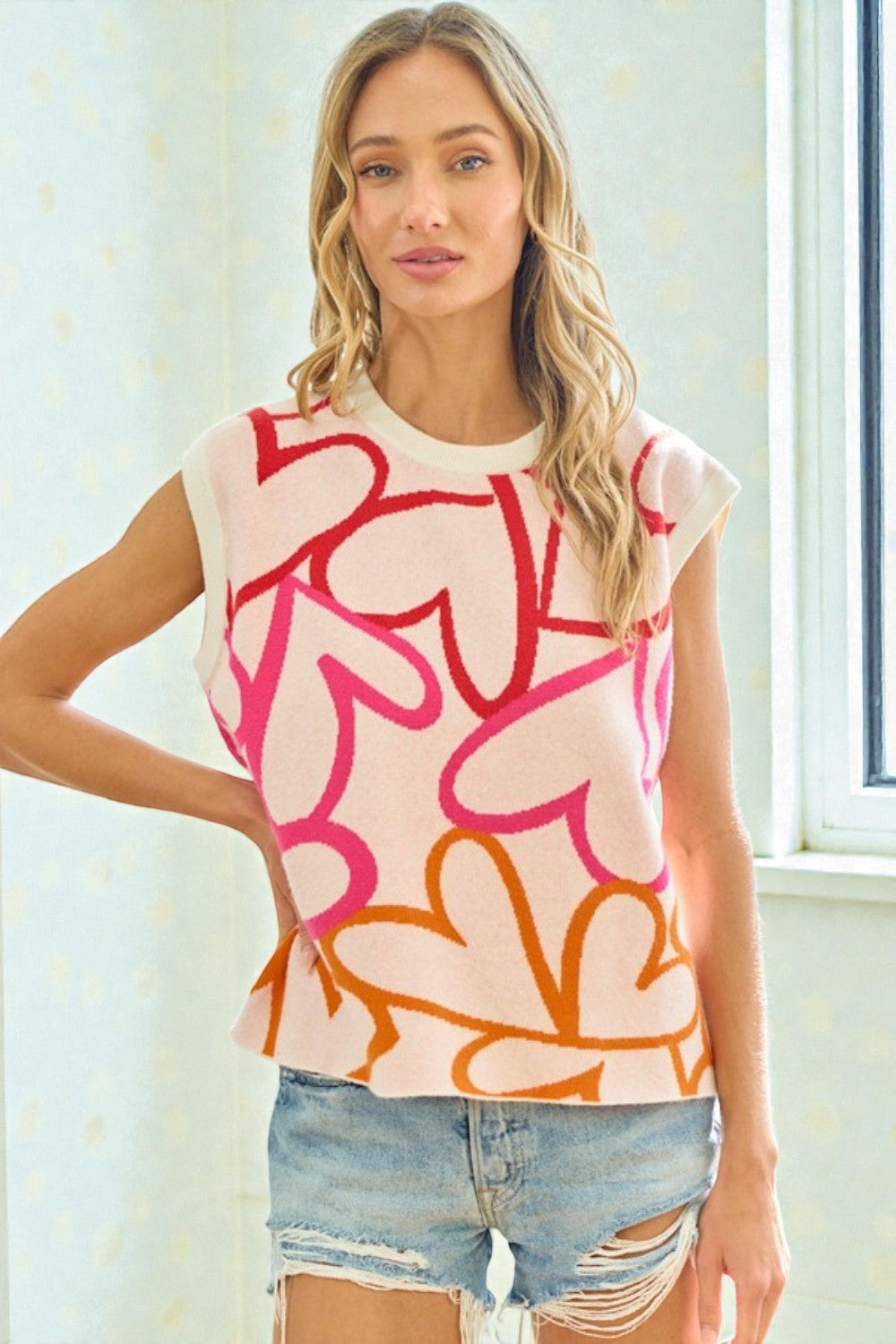Woman wearing a sleeveless top with abstract pink and orange design and denim shorts indoors.