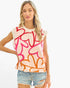A woman modeling a sleeveless knit top with a cream base and an abstract pattern of overlapping hearts in red, pink, and orange, paired with distressed denim shorts against a plain white background.