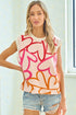 Woman wearing a sleeveless top with abstract pink and orange design and denim shorts indoors.