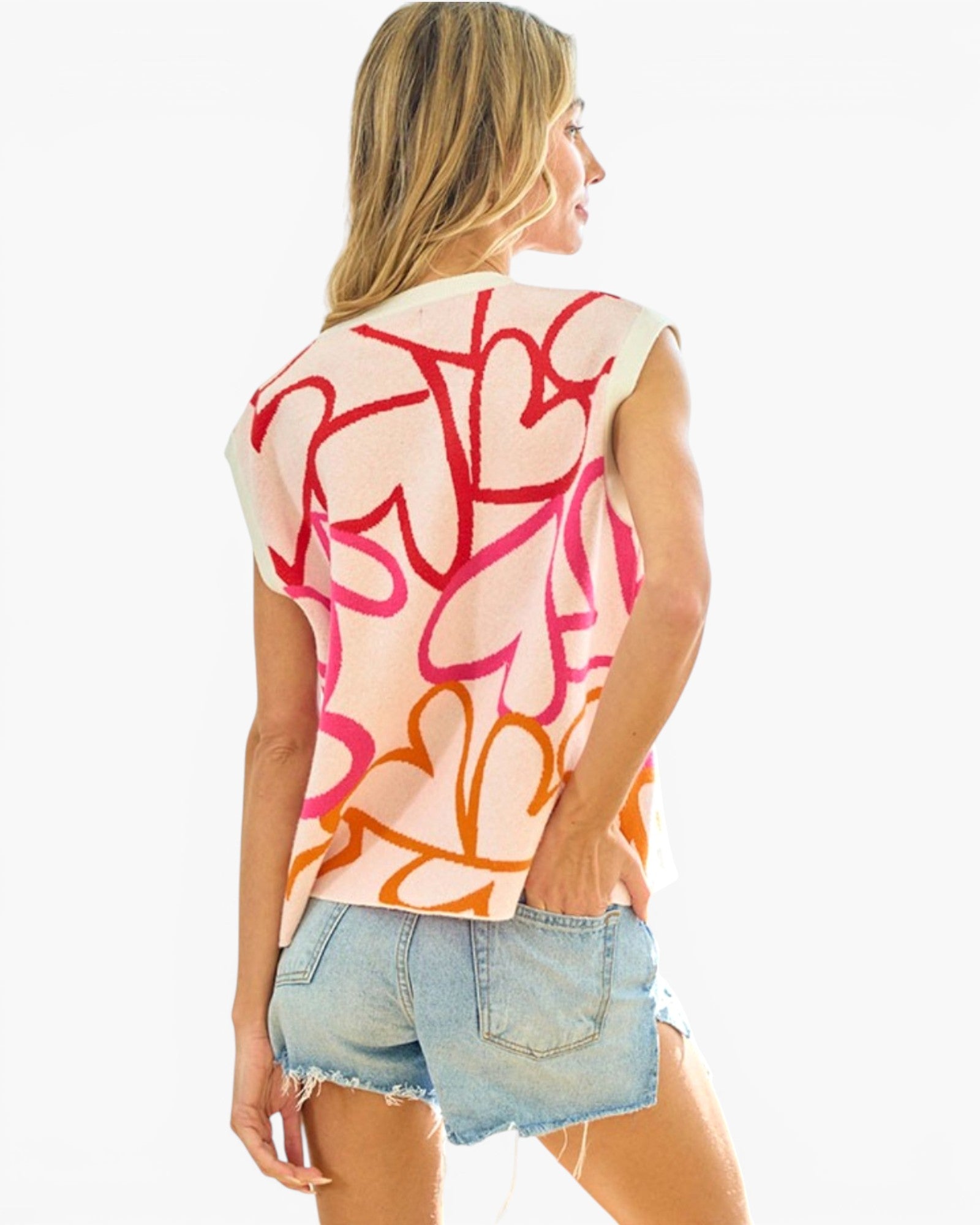 A woman shown from the back wearing a sleeveless top with an abstract graffiti-style pattern in red, pink, and orange on a cream base, paired with light blue denim shorts against a plain white background.