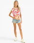 A woman modeling a sleeveless white t-shirt with a vibrant abstract graffiti-style pattern in pink, orange, and red, paired with denim shorts and white sneakers, against a solid white background.
