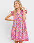 A woman modeling a tiered V-neck dress with a vibrant abstract print in pink, orange, yellow, green, and blue, set against a plain light gray background.