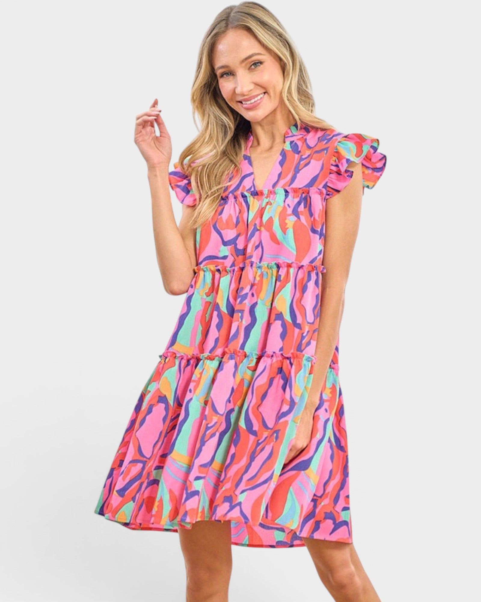 A woman modeling a tiered mini dress with a vibrant abstract print in pink, orange, teal, and purple, set against a plain light gray background.