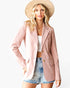 A woman modeling a light pink corduroy blazer, styled with a beige wide-brim hat, a white crop top, and denim shorts against a plain white background.