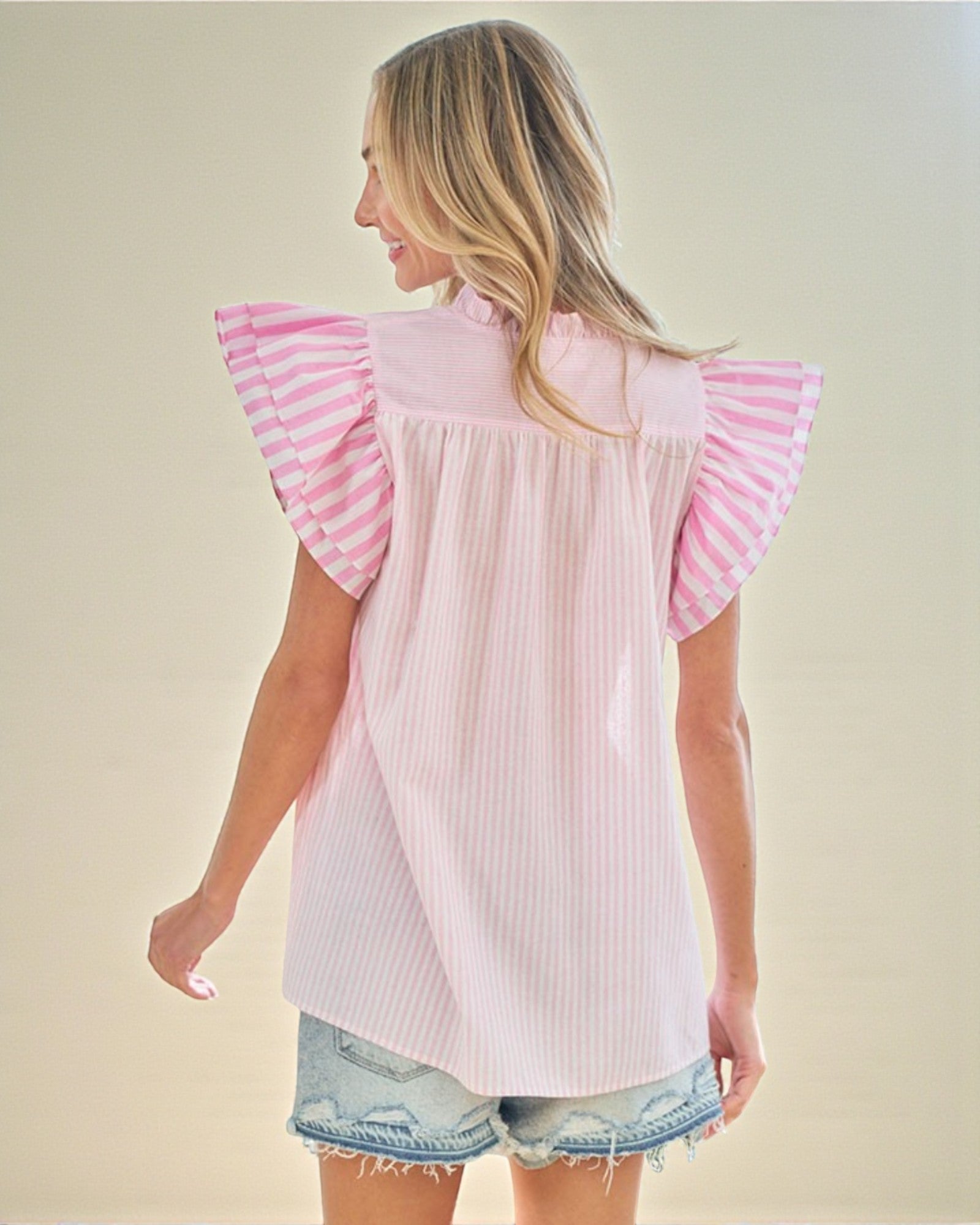 Woman wearing a light pink blouse with ruffled sleeves on a beige background
