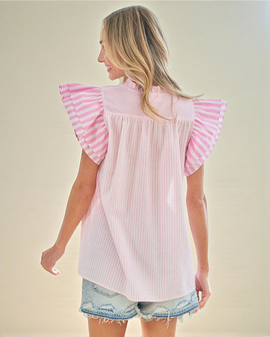 Woman wearing a light pink blouse with ruffled sleeves on a beige background