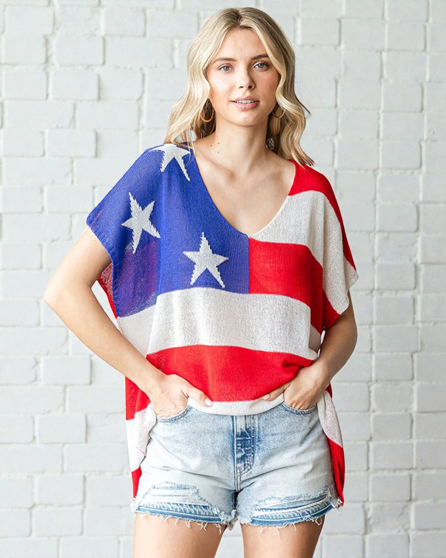 Woman wearing a colorful top with star patterns against a white brick wall.