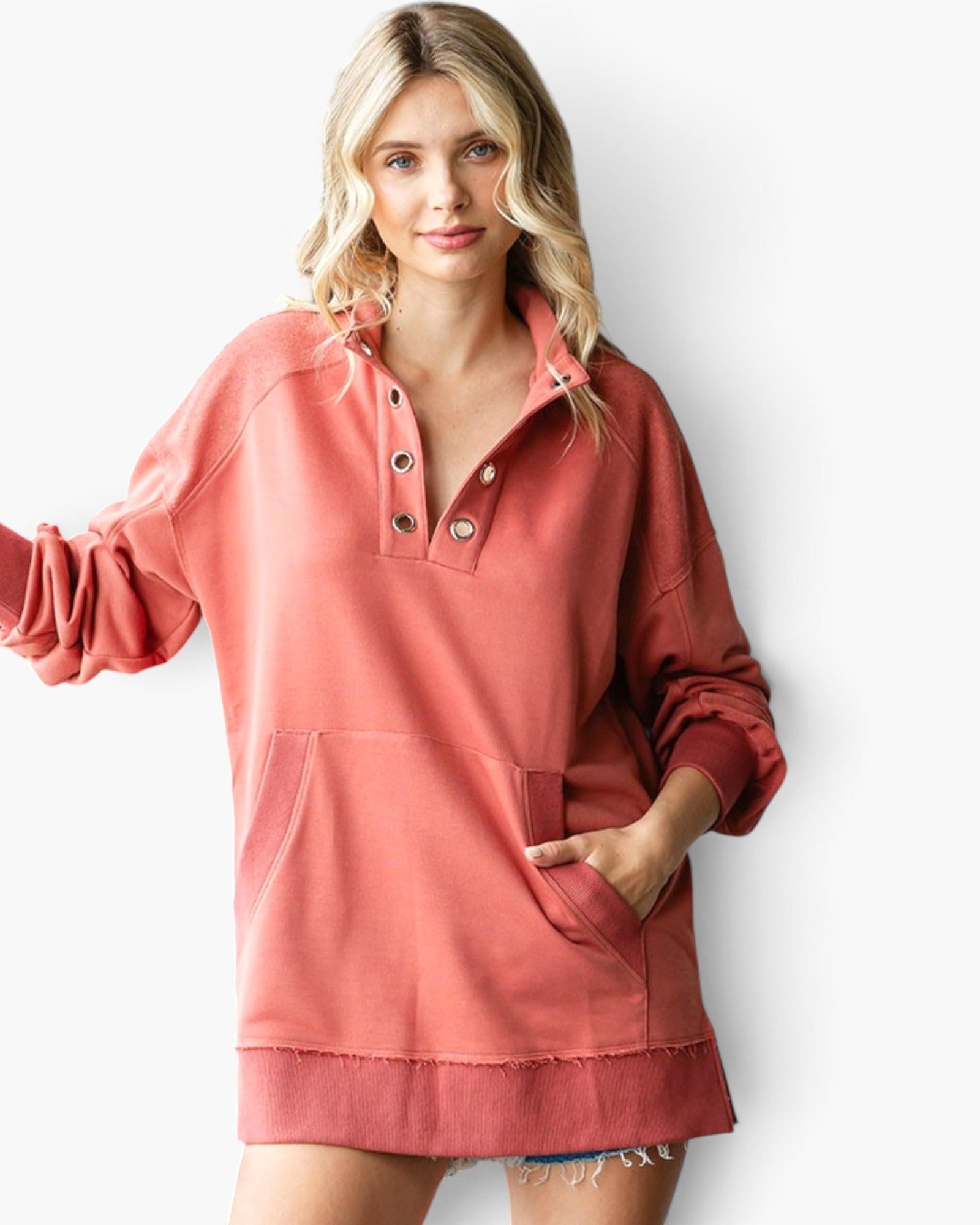 A woman modeling a dusty rose long-sleeve pullover sweatshirt with a buttoned henley collar, front pockets, and a frayed hem, set against a plain white studio background.