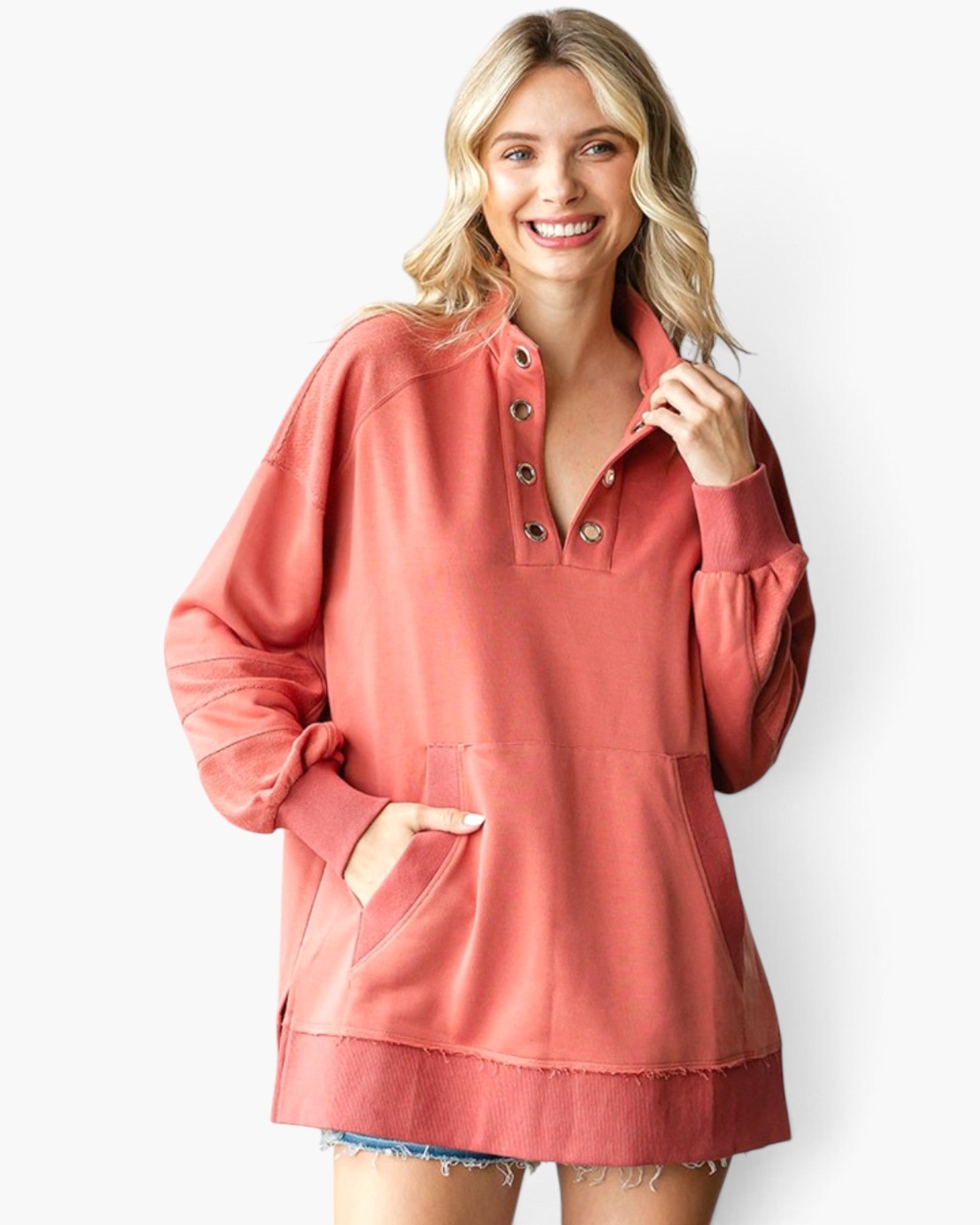 A woman wearing a dusty coral pink long-sleeve button-up pullover sweatshirt with a split kangaroo pocket, shown against a plain white studio background.
