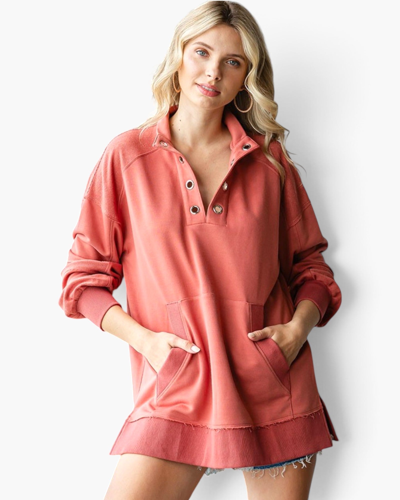 A woman wearing a coral pink long-sleeve button-up sweatshirt with a relaxed fit, front pockets, and a raw hem, photographed against a clean white background.