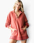 A woman wearing a coral pink long-sleeve button-up sweatshirt with a relaxed fit, front pockets, and a raw hem, photographed against a clean white background.