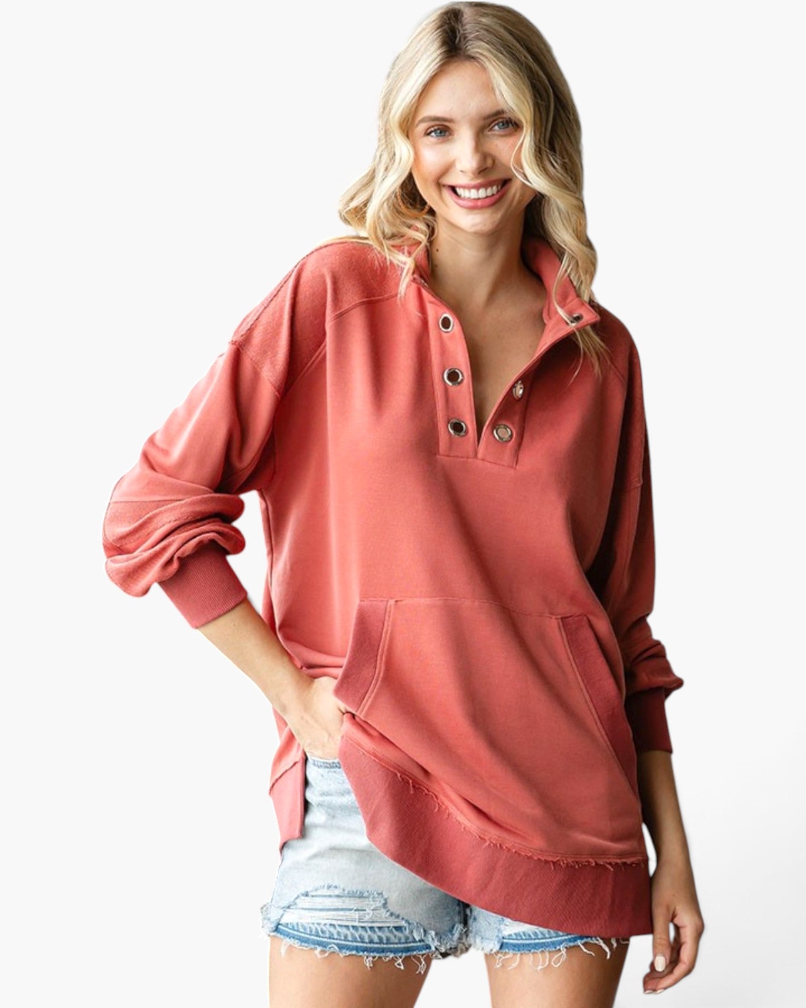 A woman wearing a dusty rose long-sleeve quarter-placket pullover sweatshirt with denim shorts, standing against a plain white studio background.