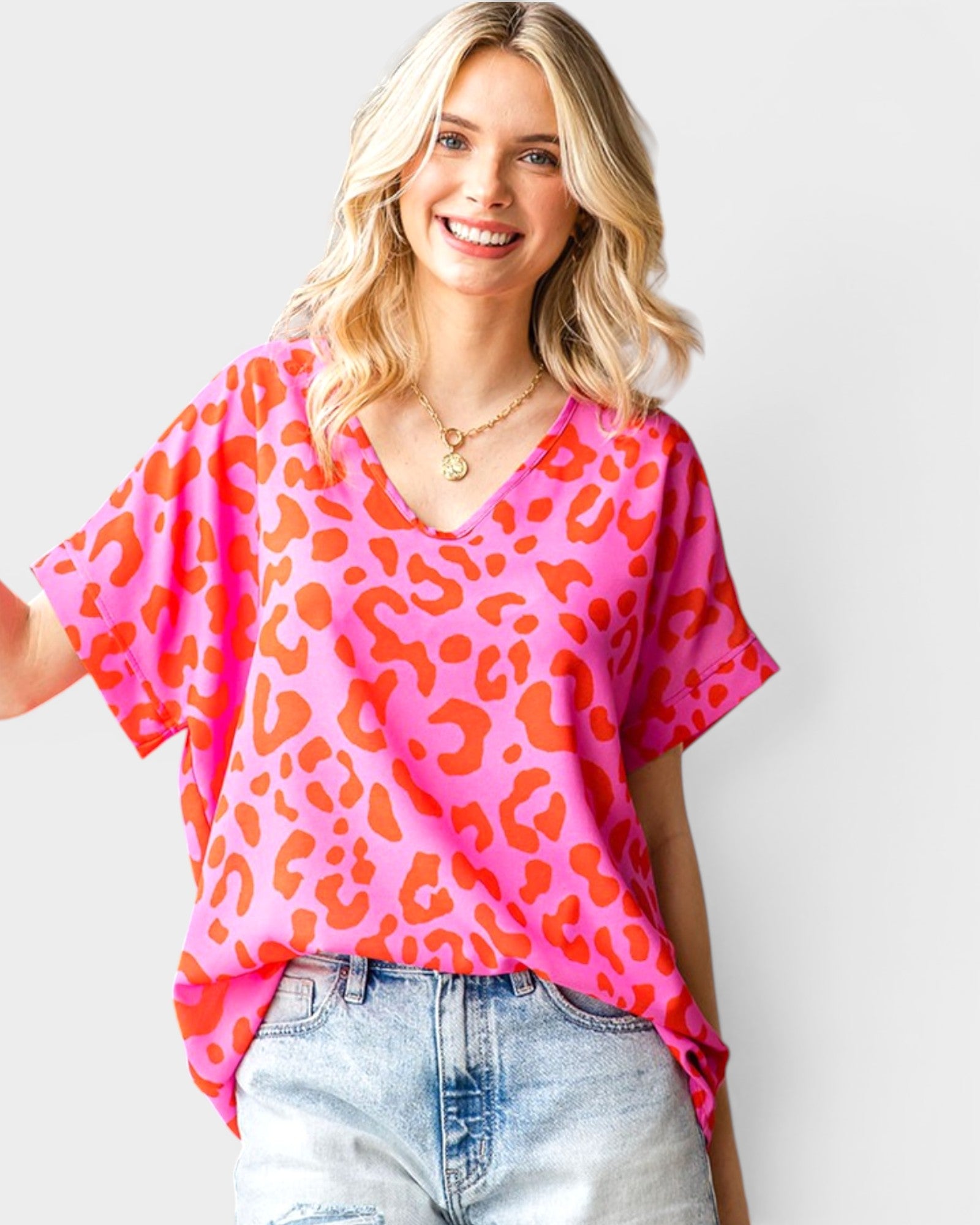 Woman wearing a pink leopard print top and light blue jeans against a white background
