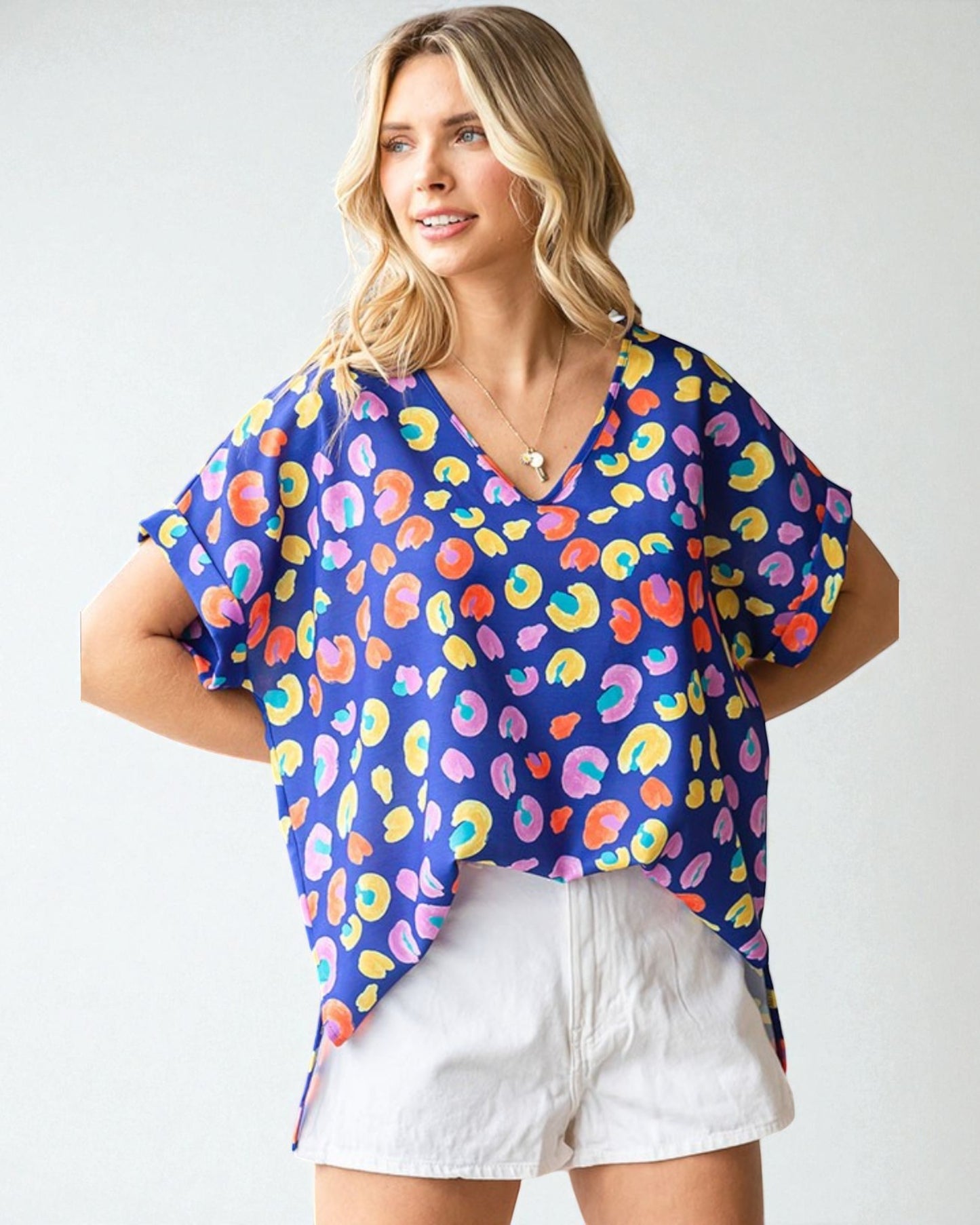 Woman wearing a colorful patterned top and white shorts on a plain background