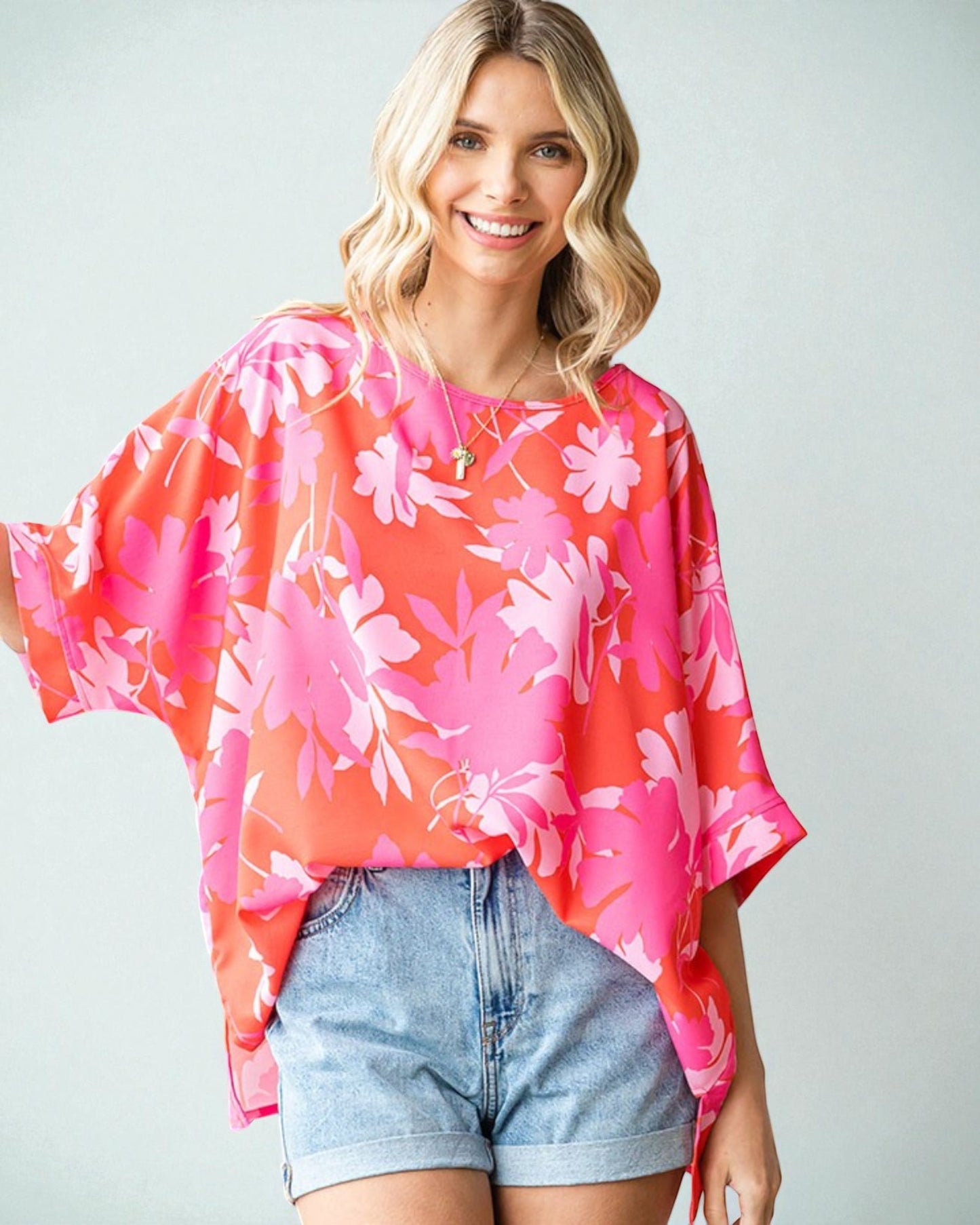 Woman wearing a pink floral kimono-style top and denim shorts on a plain background