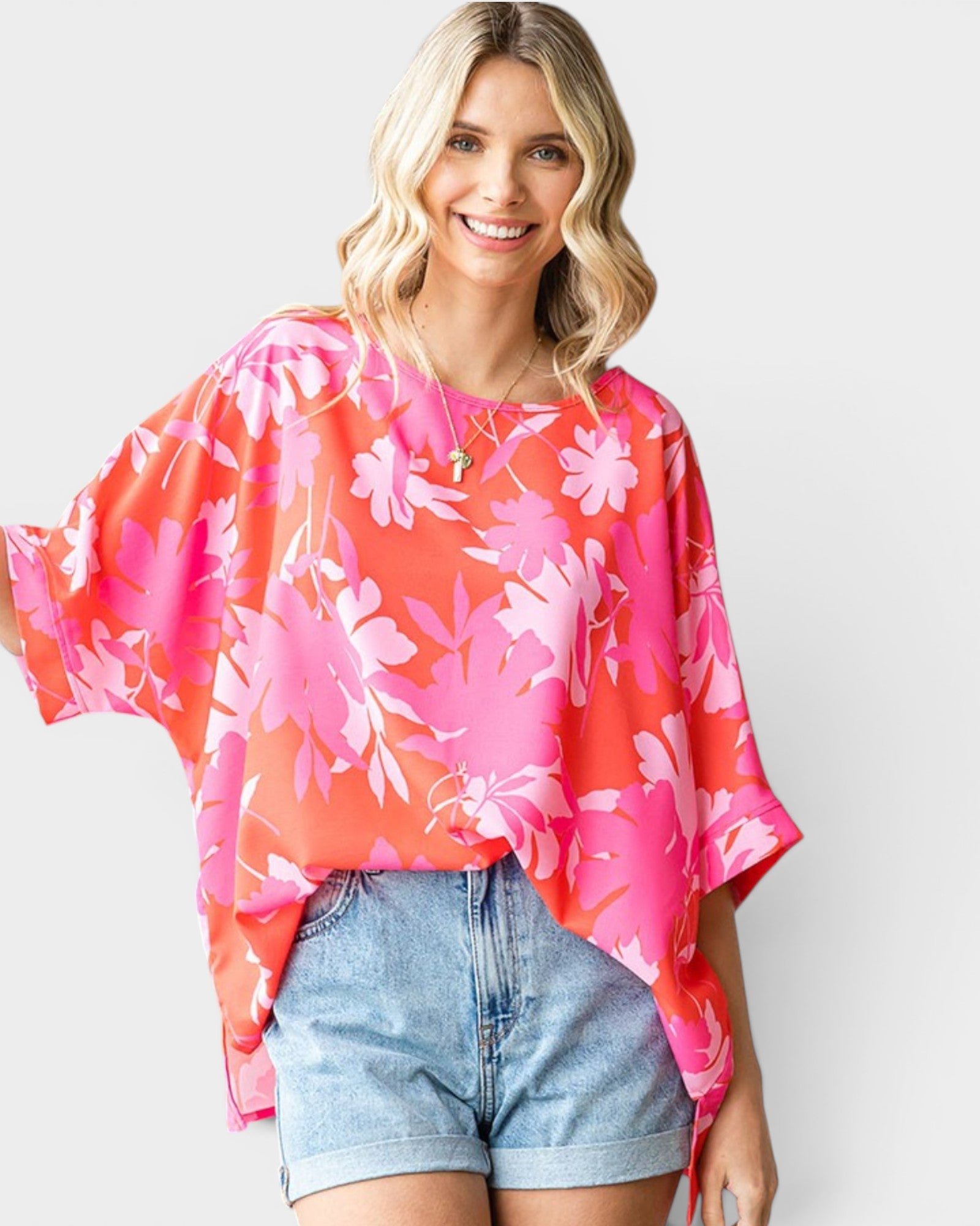 Woman wearing a pink floral blouse and denim shorts on a plain background