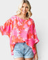 Woman wearing a pink floral blouse and denim shorts on a plain background