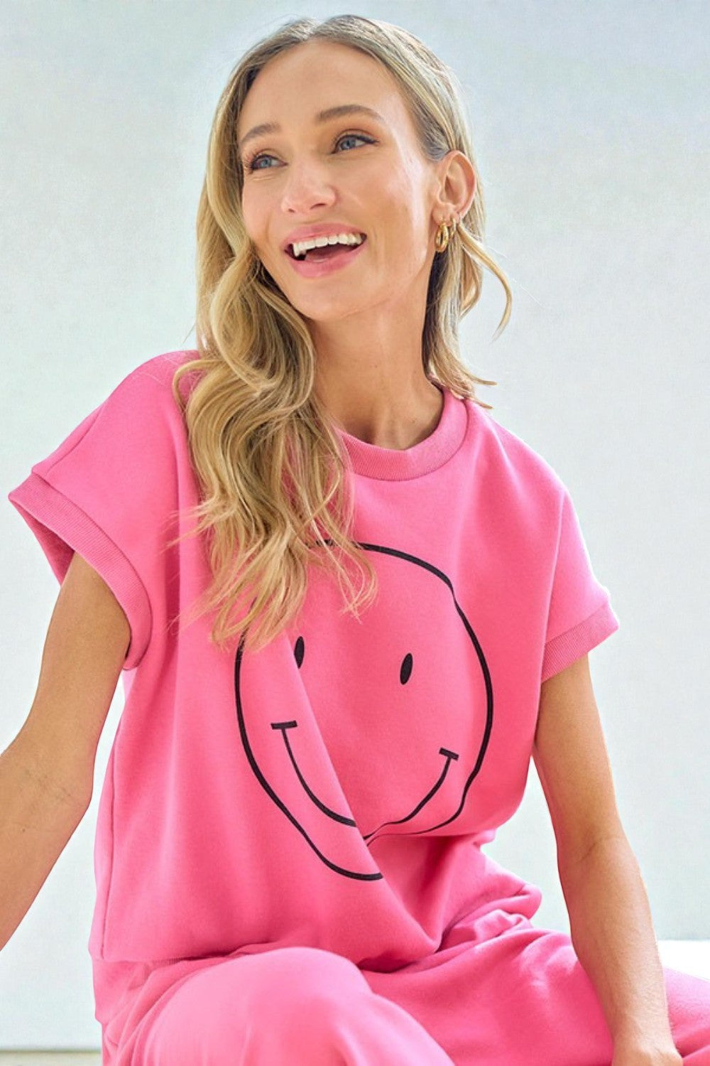 Woman wearing a pink outfit with a smiley face design on a light background